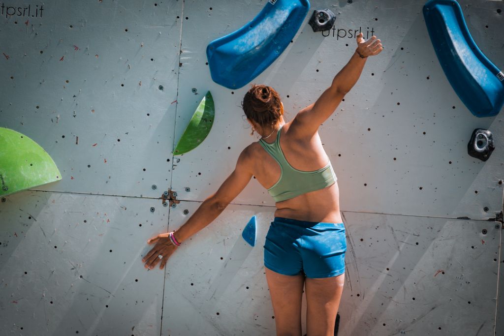 Atleta di spalle sulla parete chiara con prese blu e verdi